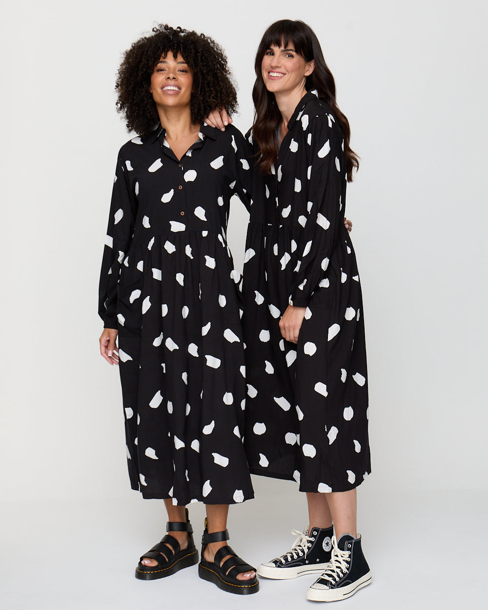 Two women wearing black dresses with white patterns on a white background