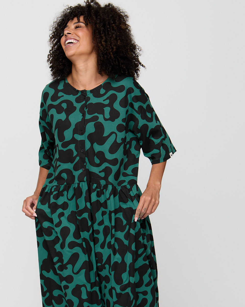 Woman wearing a green and black patterned dress on a plain background