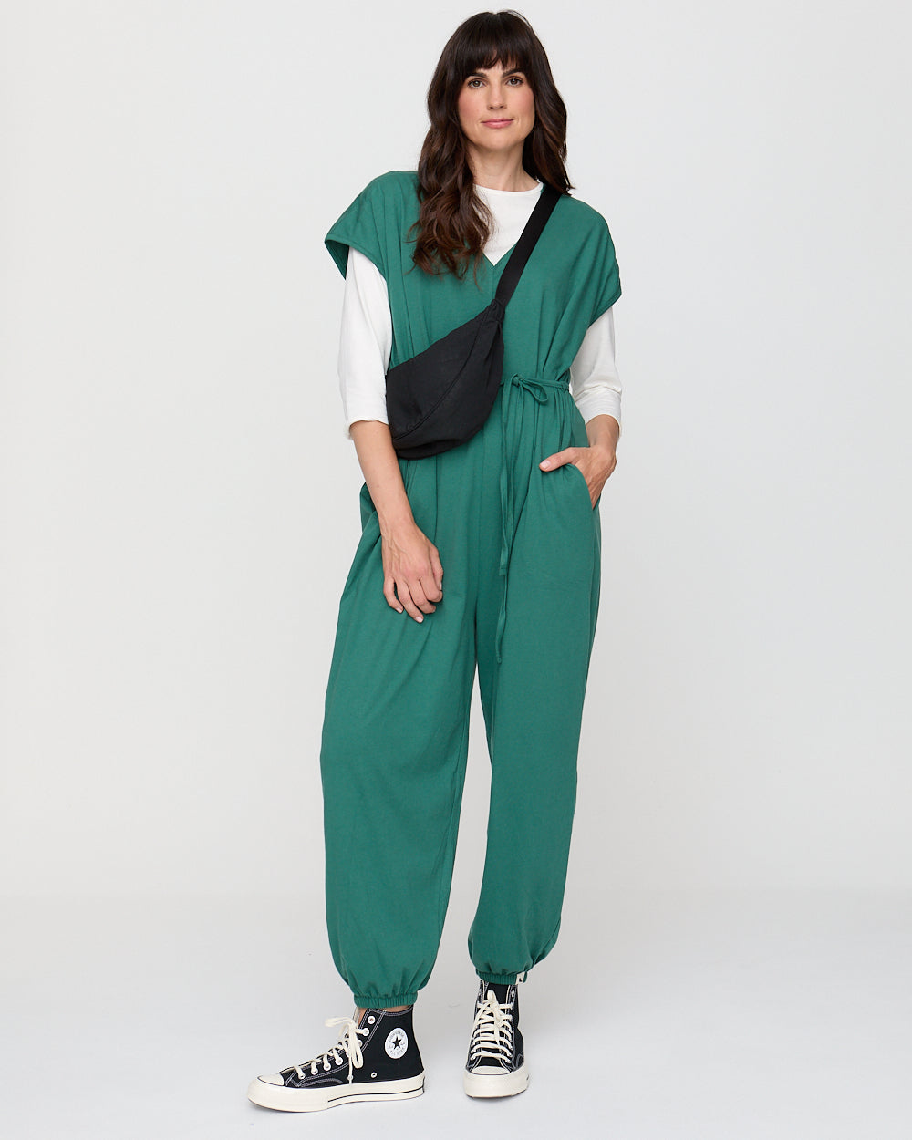 Woman wearing a green jumpsuit with a white shirt underneath on a white background