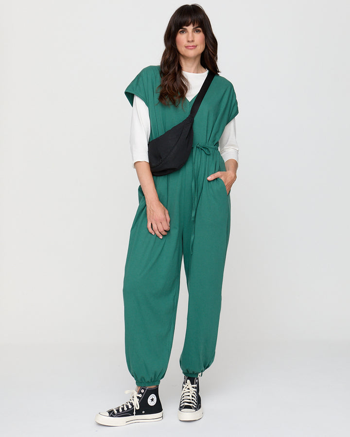Woman wearing a green jumpsuit with a white shirt underneath on a white background