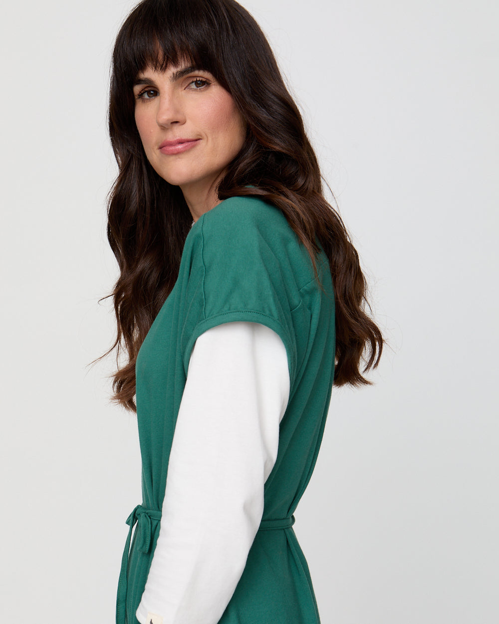 Woman wearing a green dress with a white shirt underneath on a light gray background