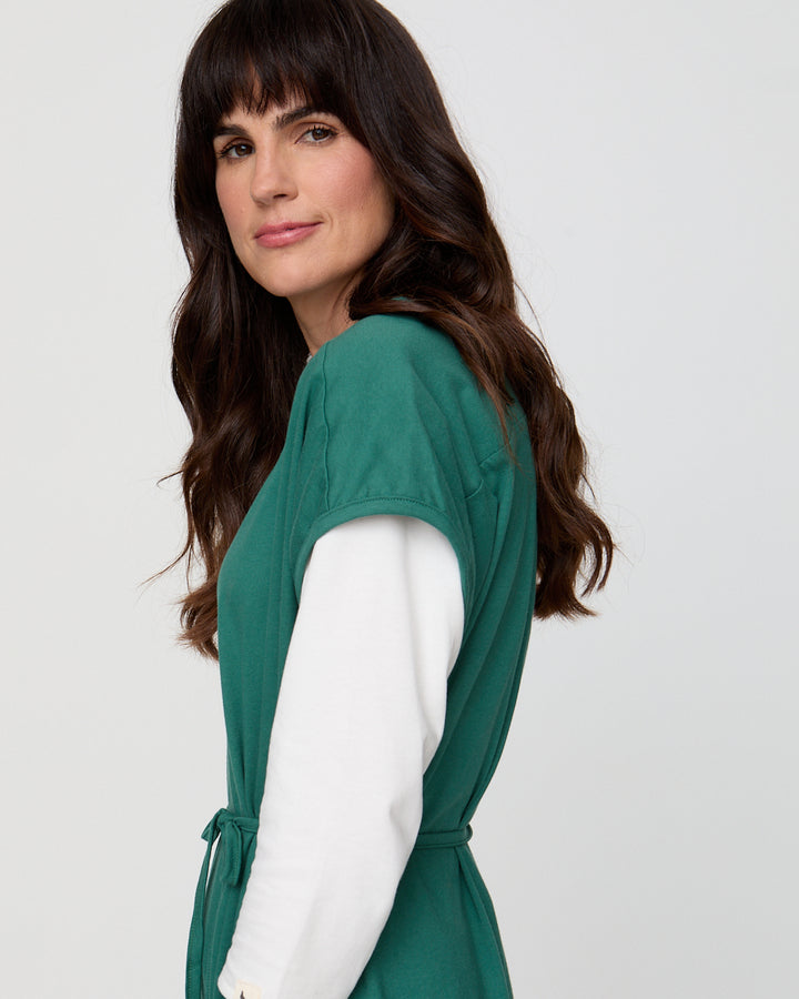 Woman wearing a green dress with a white shirt underneath on a light gray background
