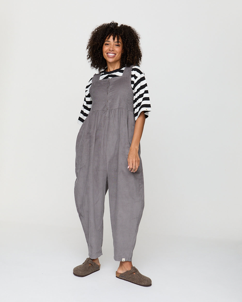 Woman wearing gray overalls and a striped shirt on a white background
