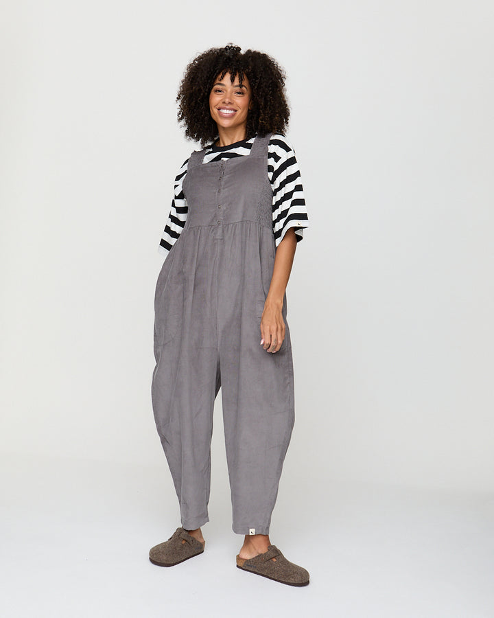 Woman wearing gray overalls and a striped shirt on a white background