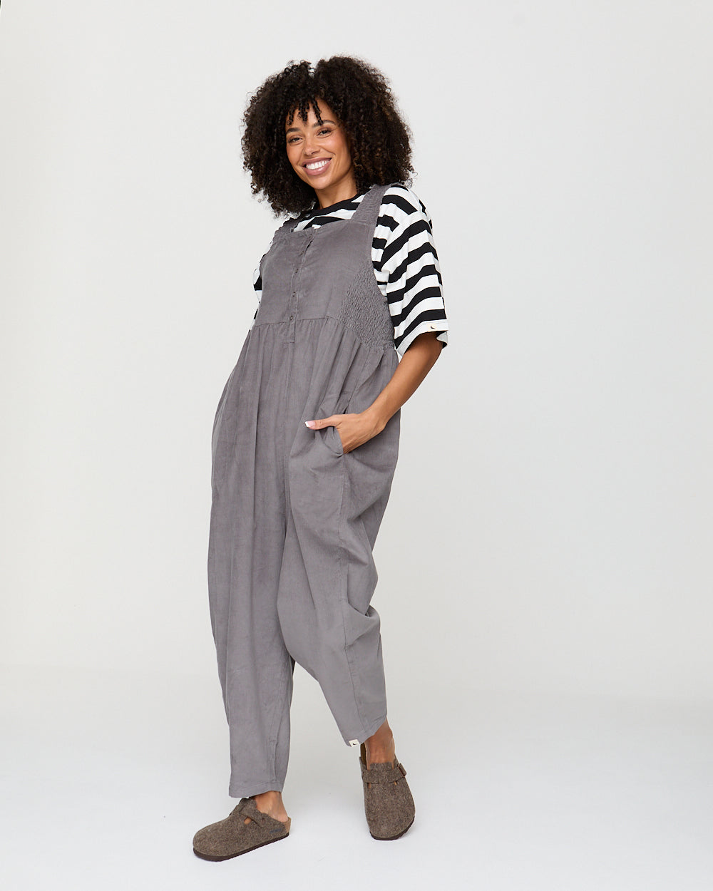 Woman wearing gray overalls and a striped shirt on a white background