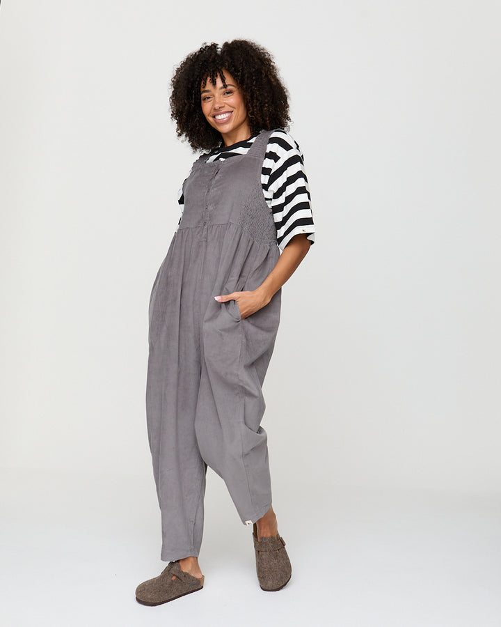 Woman wearing gray overalls and a striped shirt on a white background