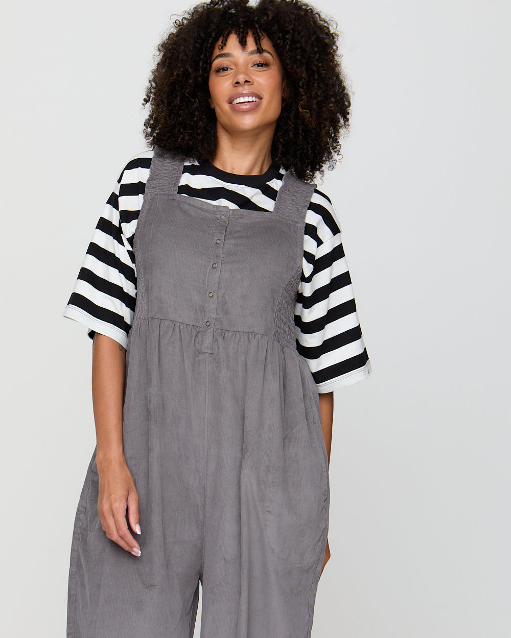 Woman wearing a gray overalls and black and white striped shirt on a plain background