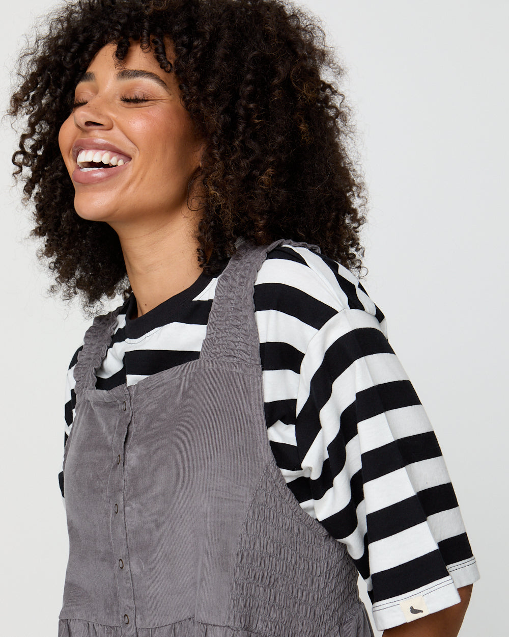 Woman wearing a black and white striped shirt with a gray apron on a plain background
