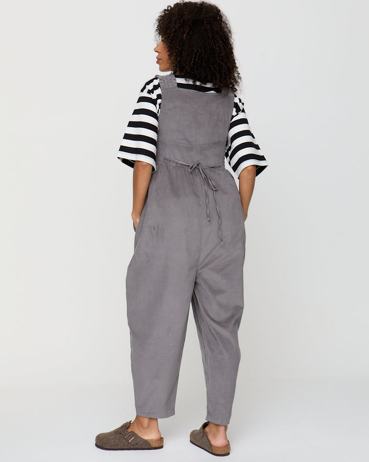 Person wearing gray overalls and a striped shirt on a white background
