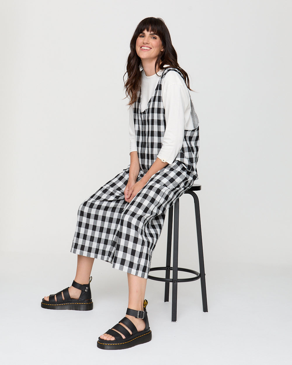Woman wearing a black and white checkered dress sitting on a stool against a white background
