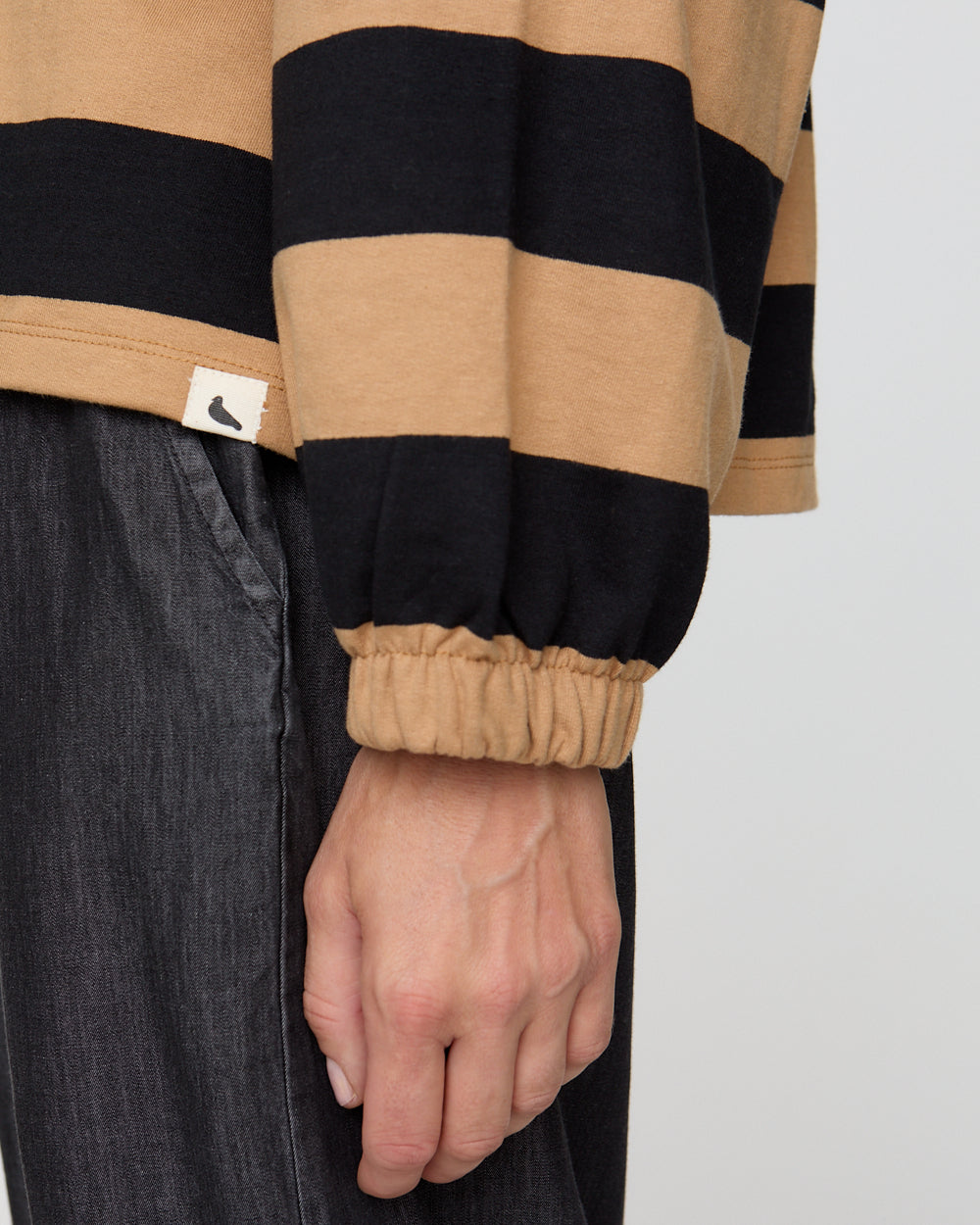 Close-up of a person wearing a black and beige striped shirt with a visible brand logo.