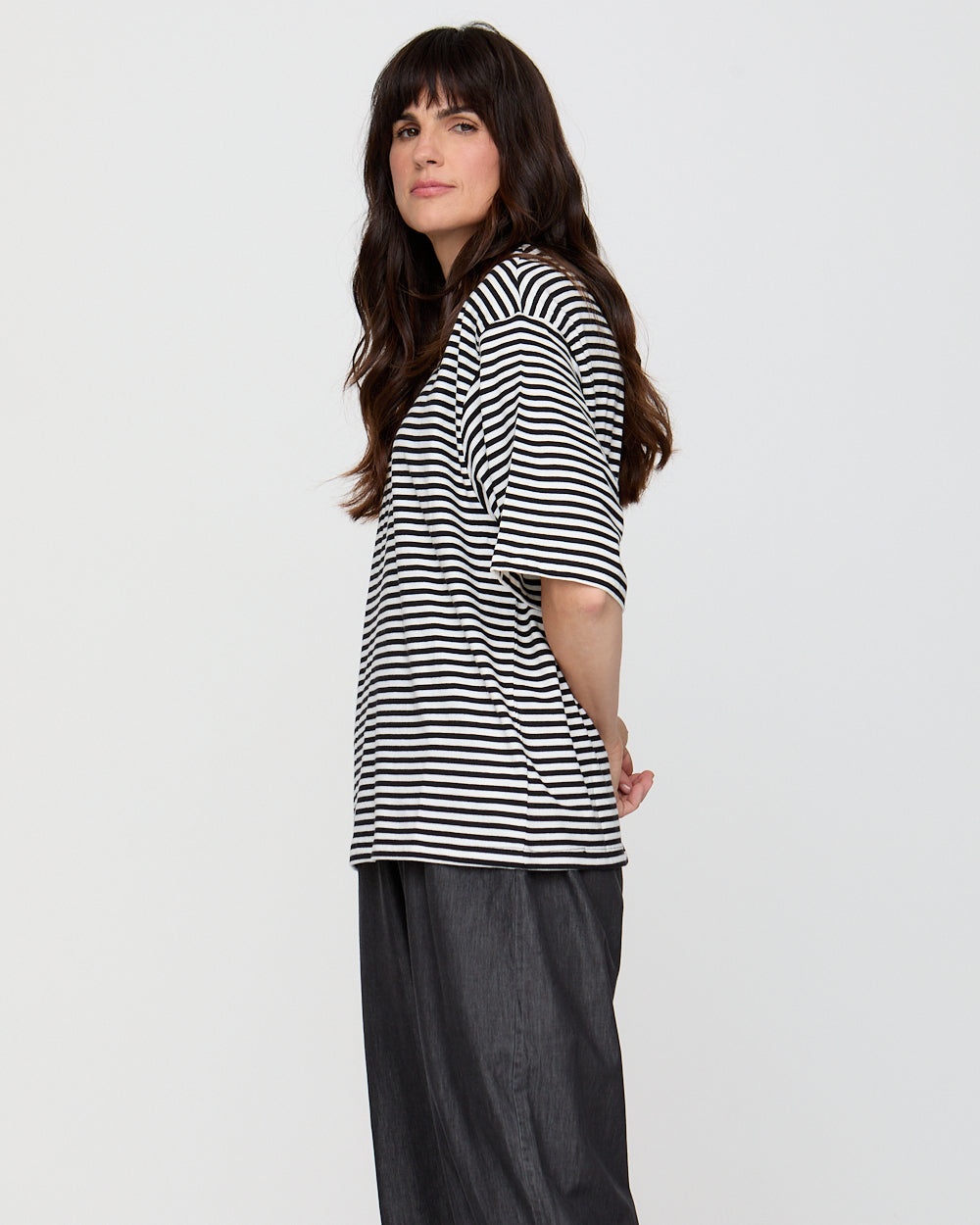 Woman wearing a black and white striped shirt with dark pants on a plain background