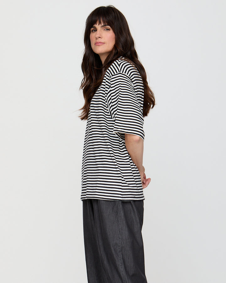 Woman wearing a black and white striped shirt with dark pants on a plain background