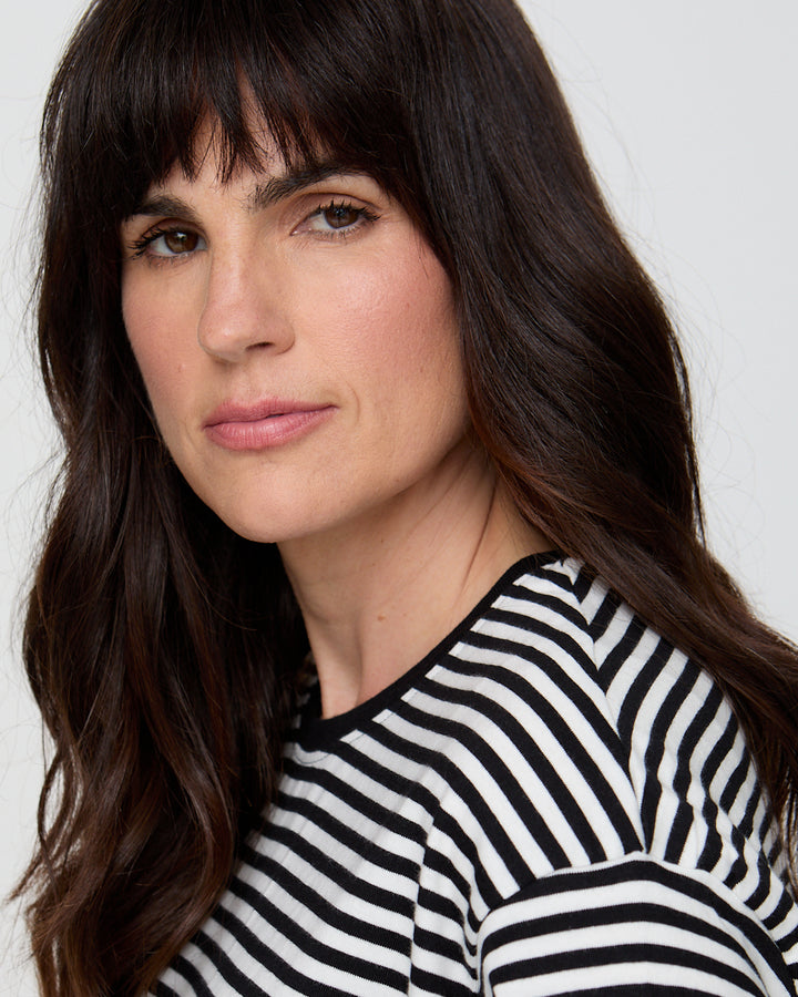 Woman with long dark hair wearing a black and white striped shirt against a plain background