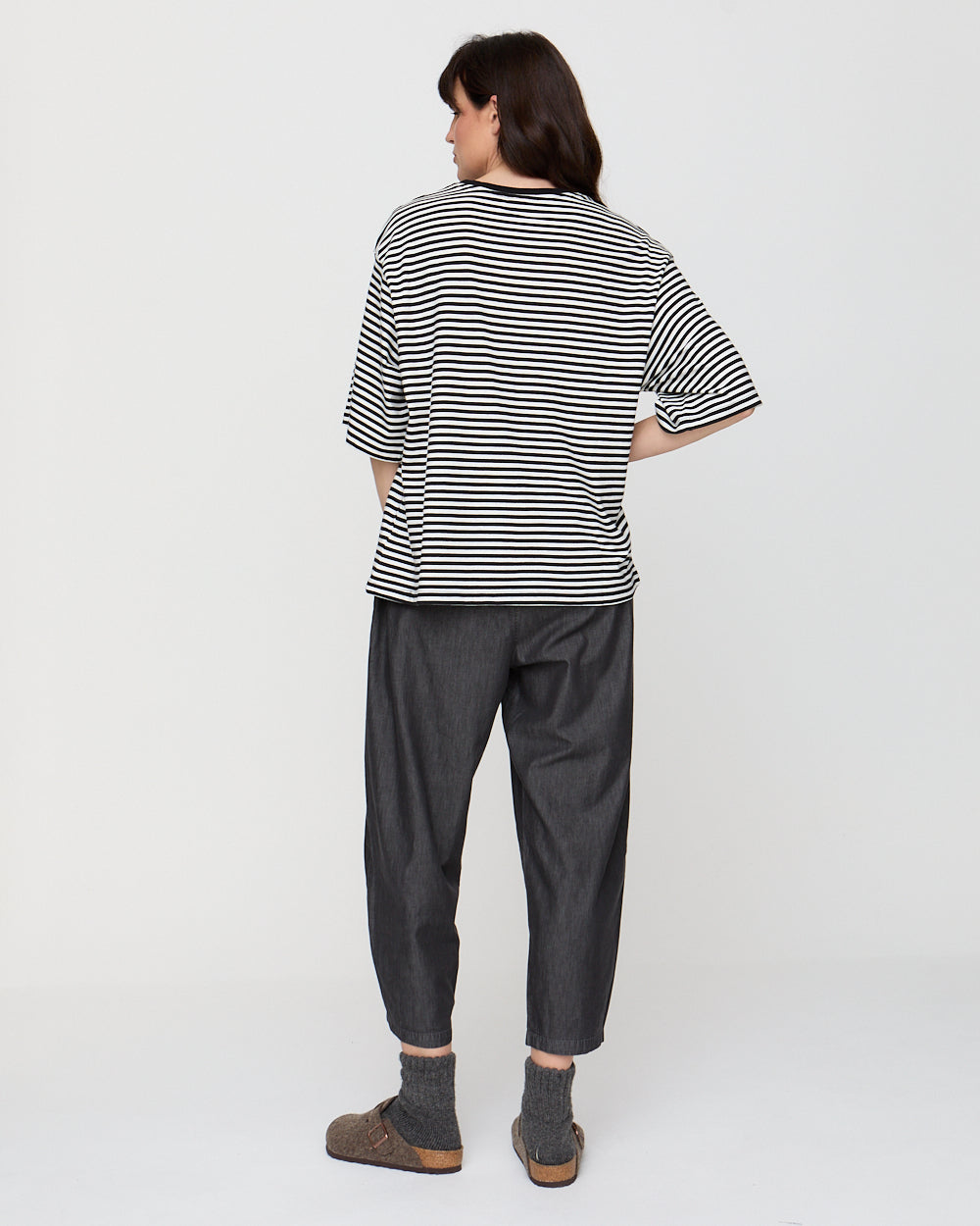 Person wearing a black and white striped shirt and dark gray pants on a white background
