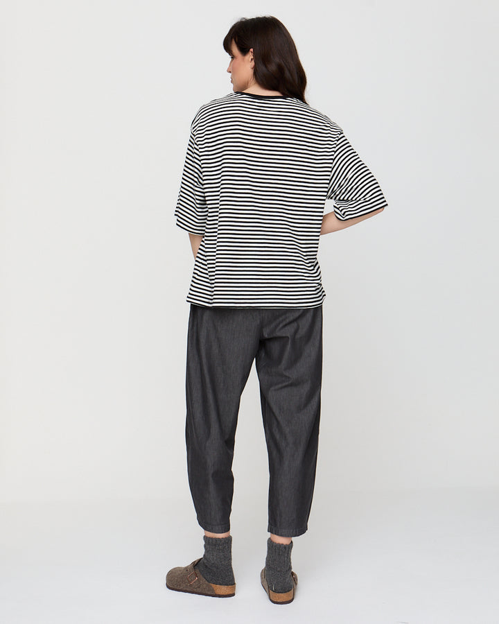 Person wearing a black and white striped shirt and dark gray pants on a white background