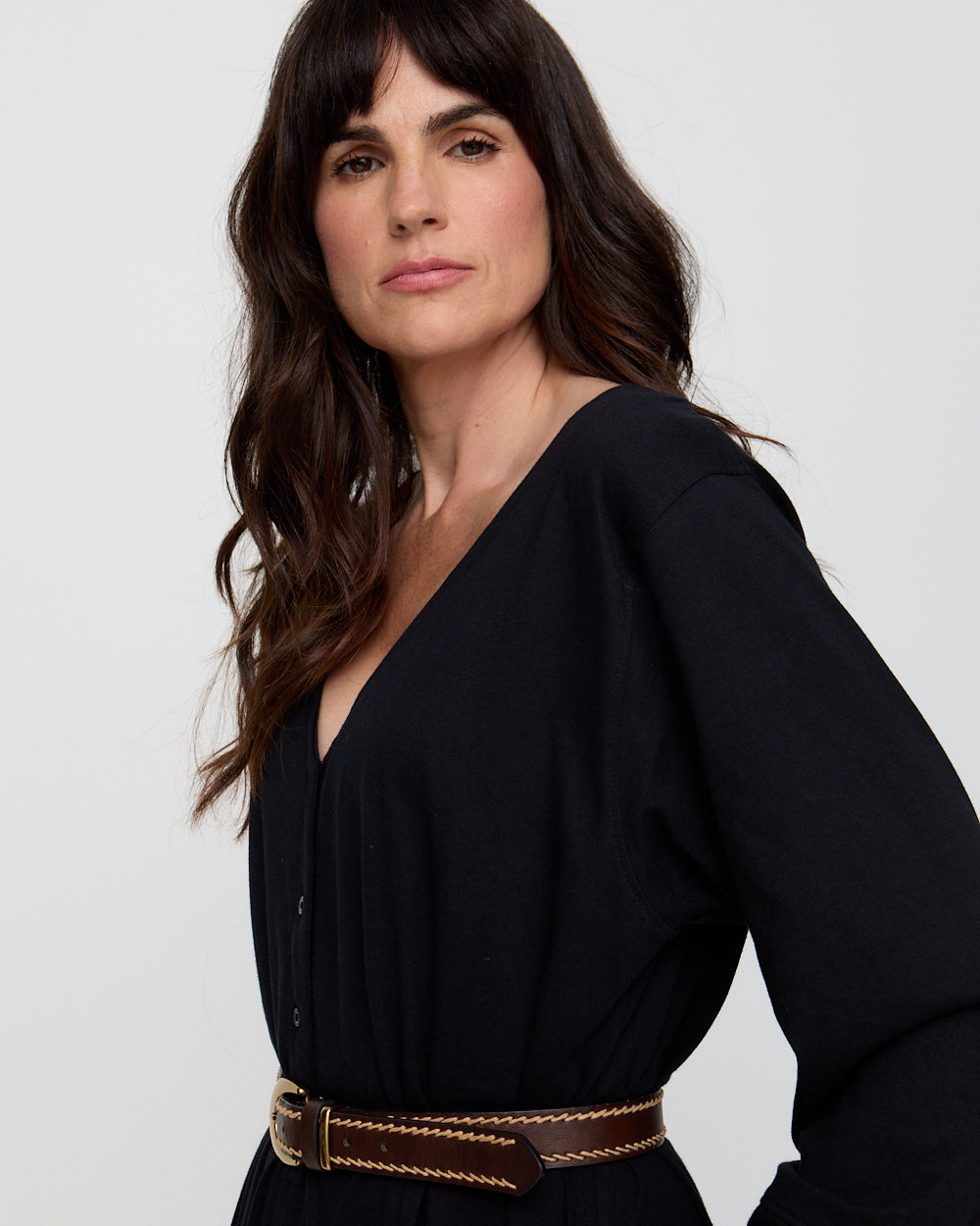 Woman wearing a black long-sleeve top with a brown belt against a white background