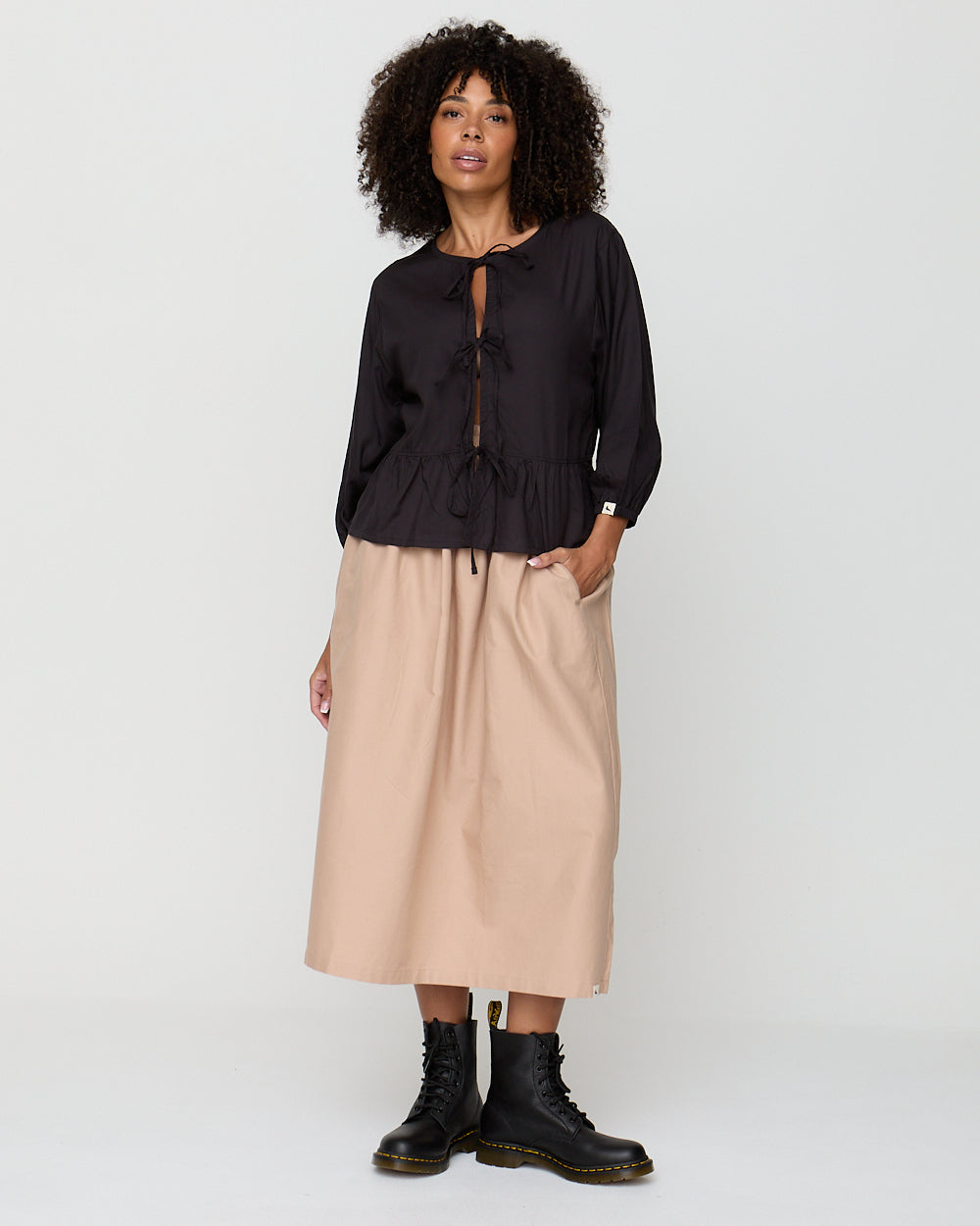 Woman wearing a black blouse and beige skirt with black boots on a white background