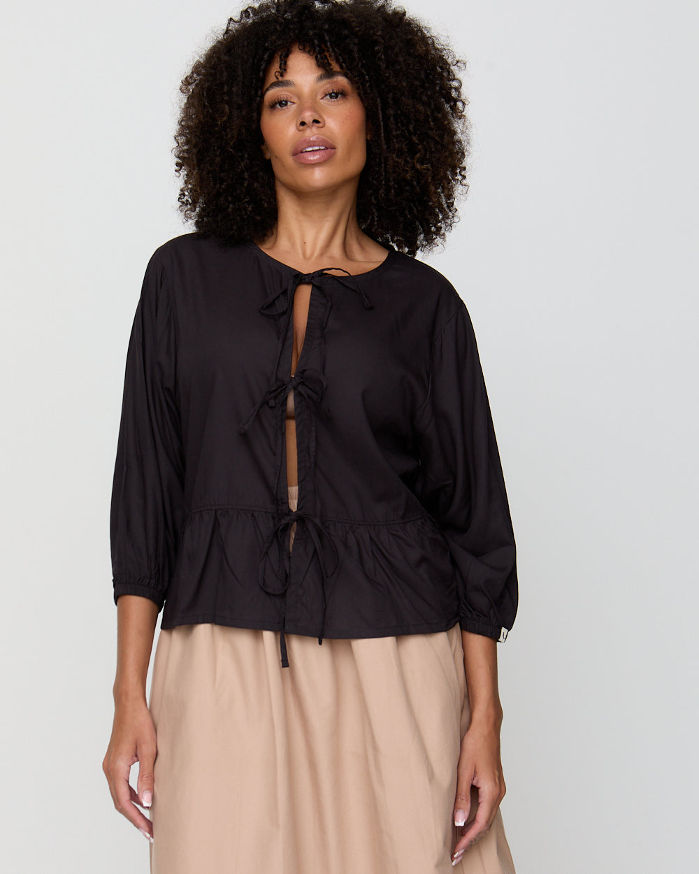 Woman wearing a black blouse with a tie detail on a plain background