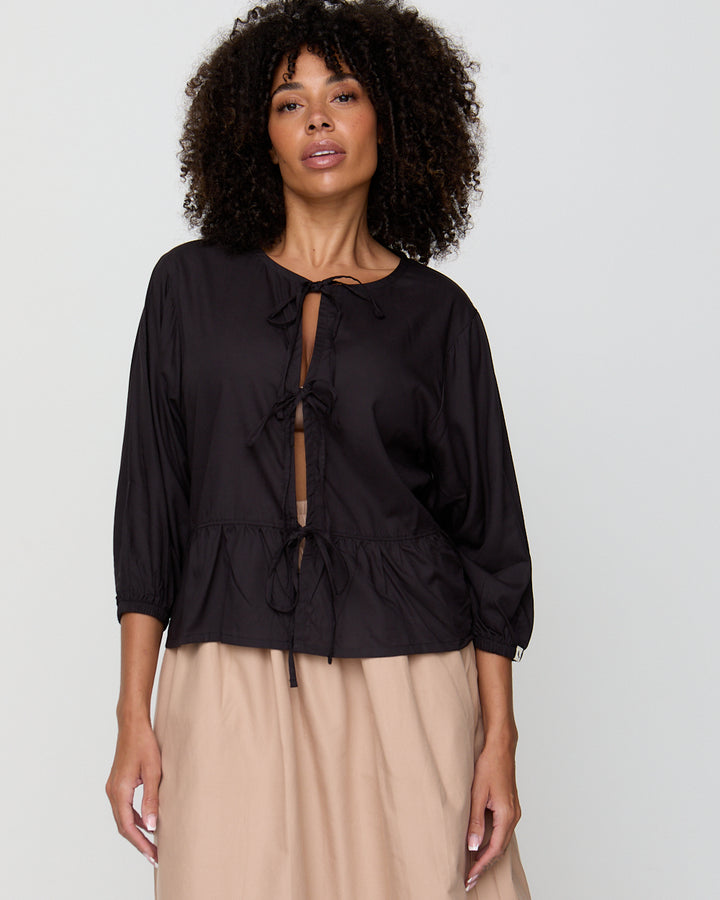 Woman wearing a black blouse with a tie detail on a plain background