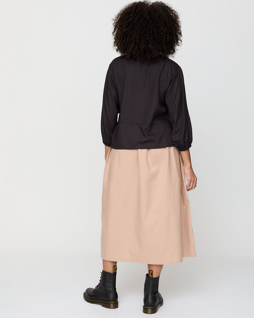 Person wearing a black top and beige skirt on a white background