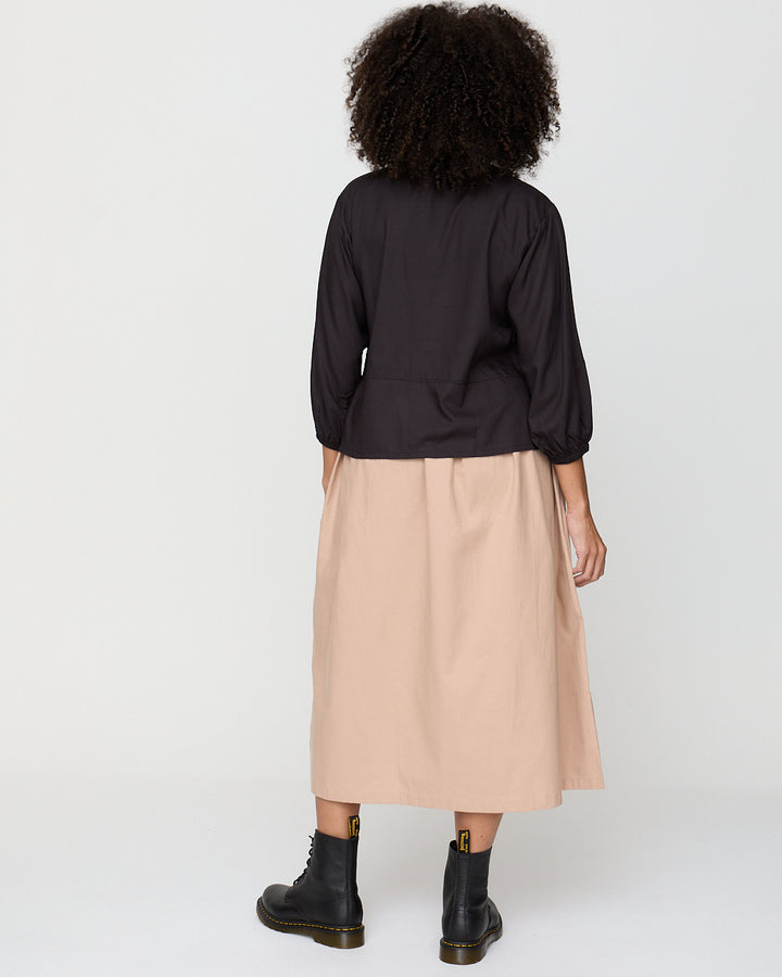 Person wearing a black top and beige skirt on a white background
