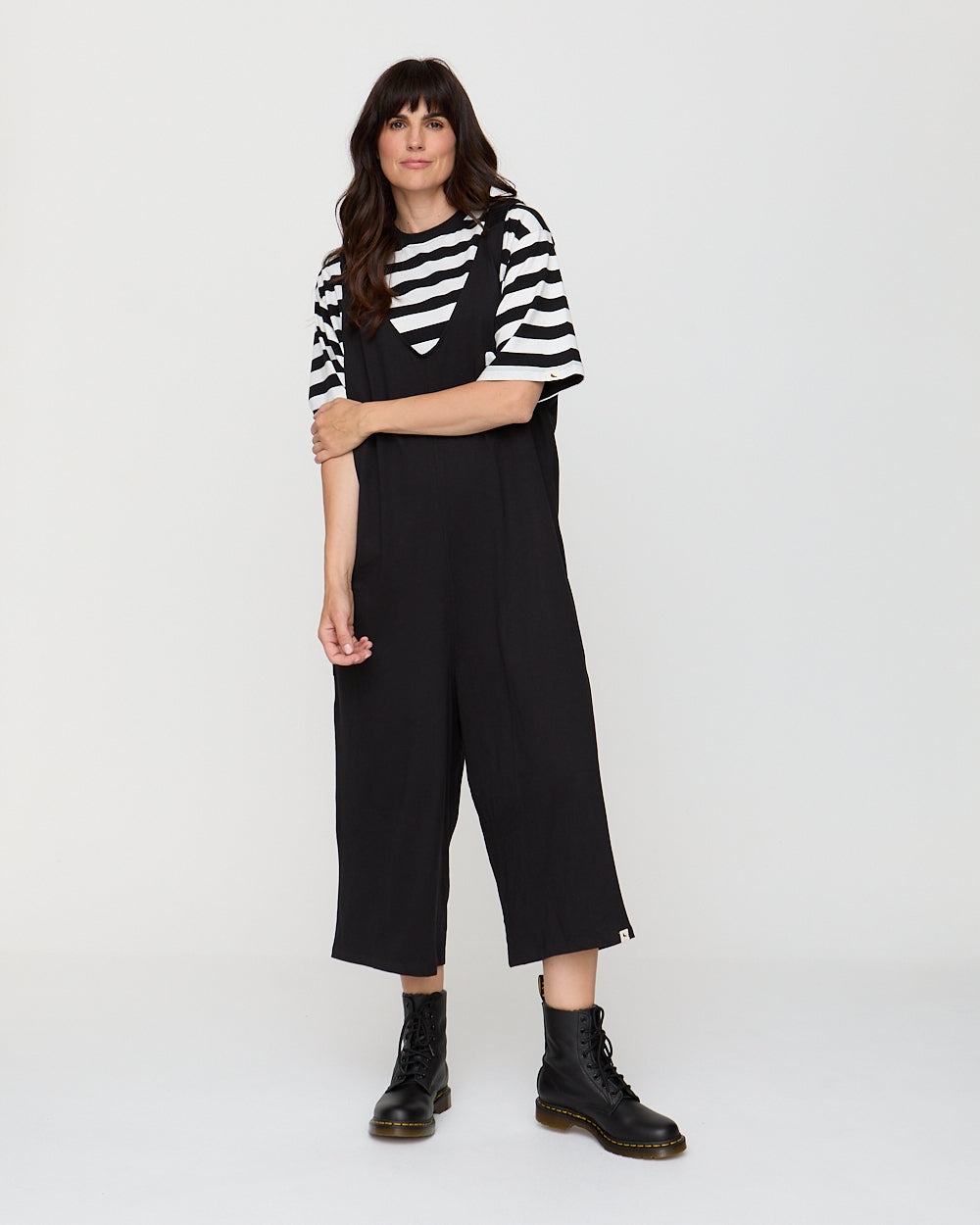 Woman wearing a black and white striped shirt with black overalls on a white background