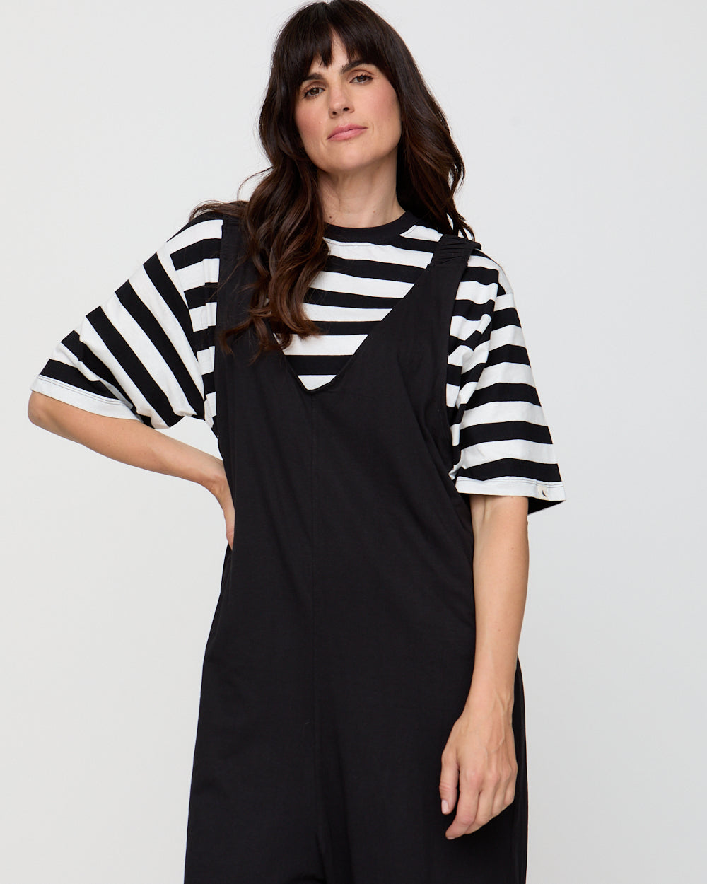 Woman wearing a black and white striped shirt with a black pinafore dress on a plain background