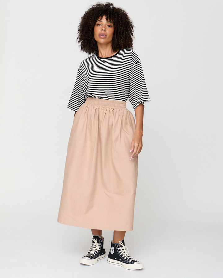 Woman wearing a striped shirt and beige skirt with black and white sneakers on a white background