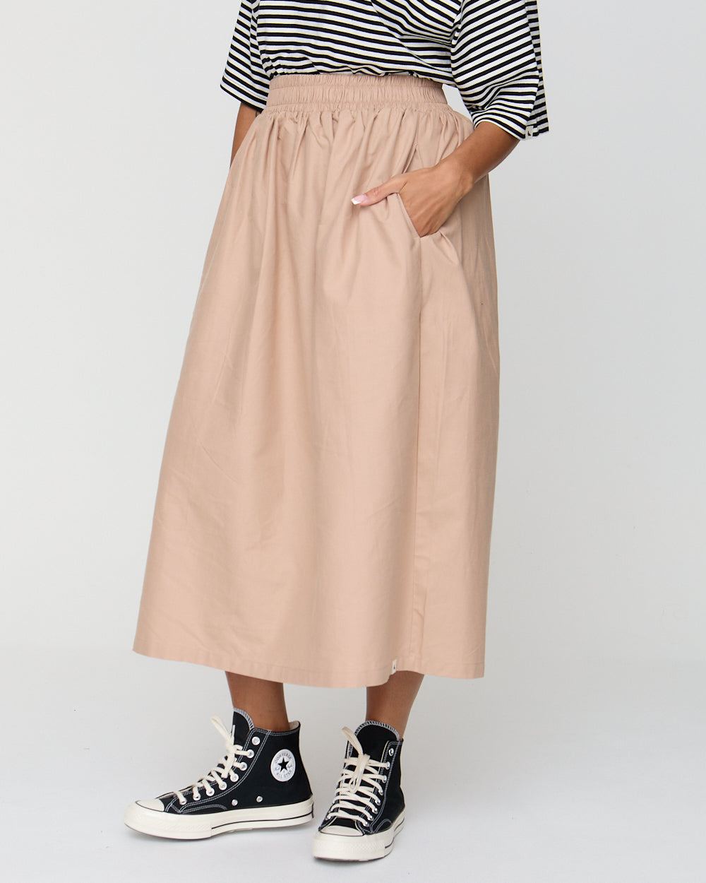 Person wearing a beige skirt, black and white striped shirt, and black high-top sneakers on a light gray background