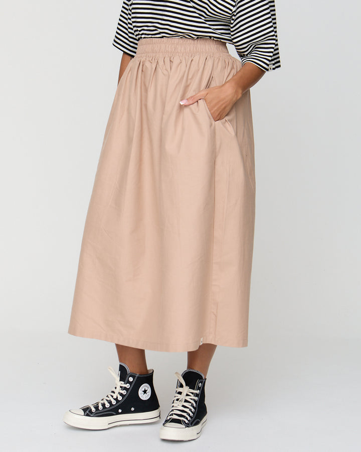 Person wearing a beige skirt, black and white striped shirt, and black high-top sneakers on a light gray background