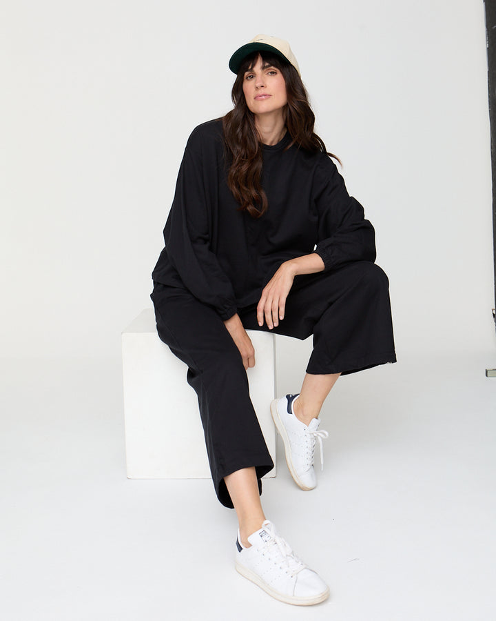 Woman wearing a black outfit with white sneakers sitting on a white chair against a white background