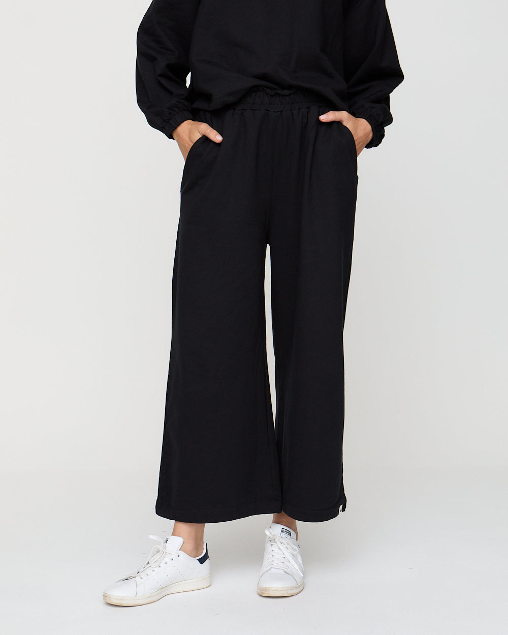 Person wearing black wide-leg pants and white sneakers on a white background