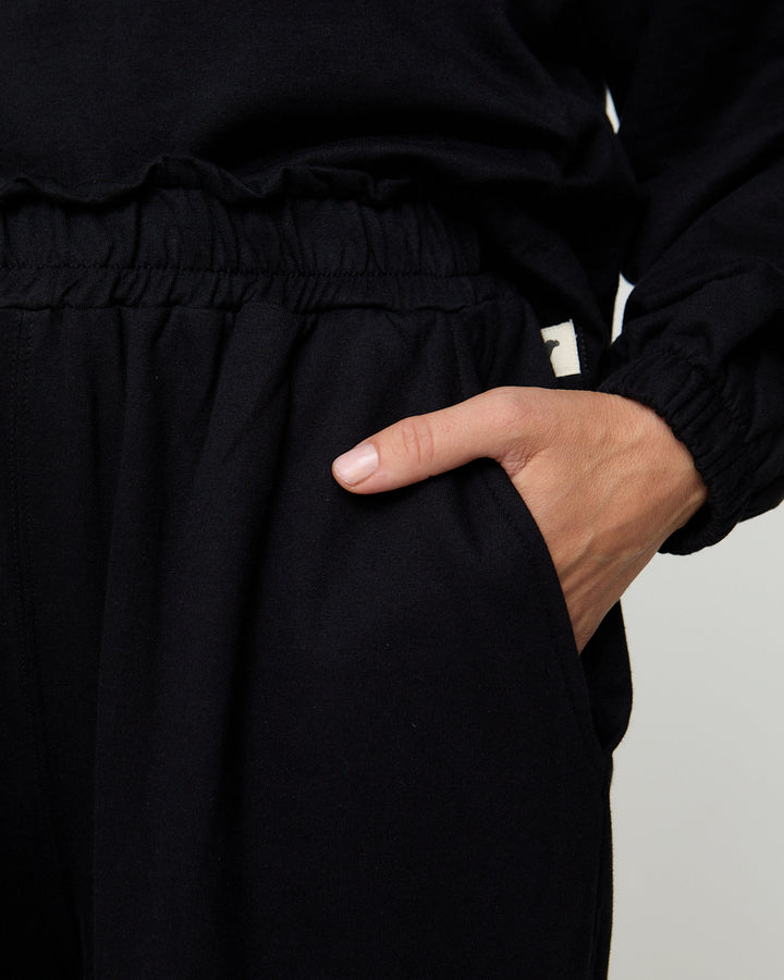 Person wearing a black outfit with a hand in the pocket against a neutral background