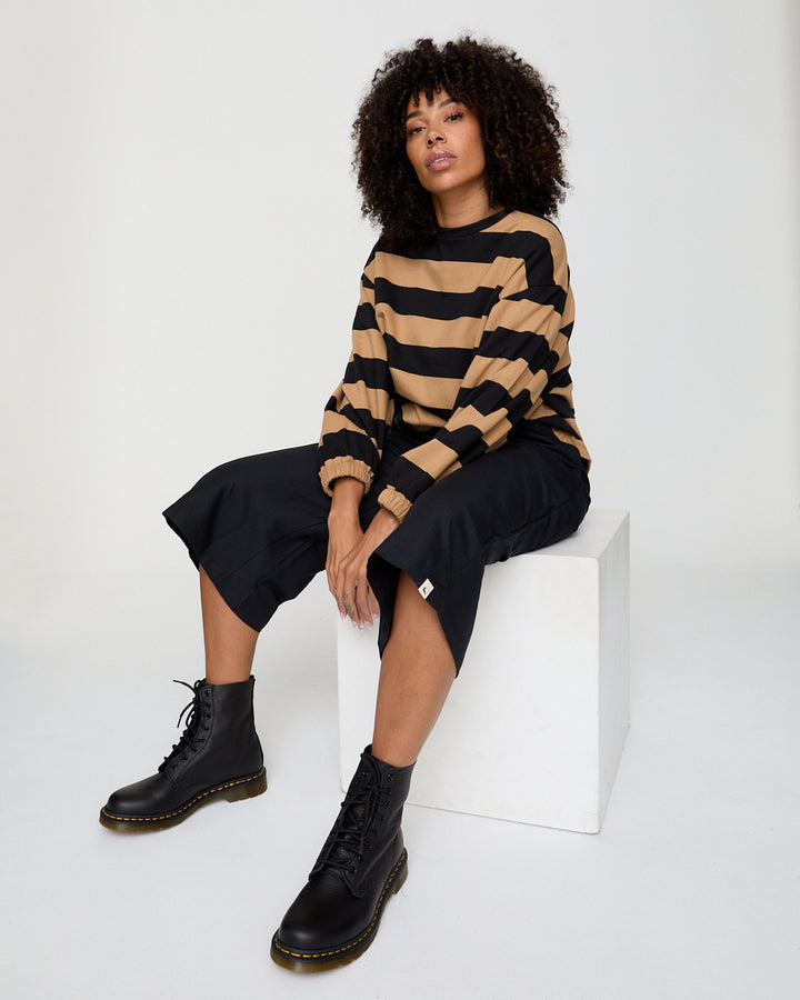 Person wearing a striped sweater and black boots sitting on a white block.