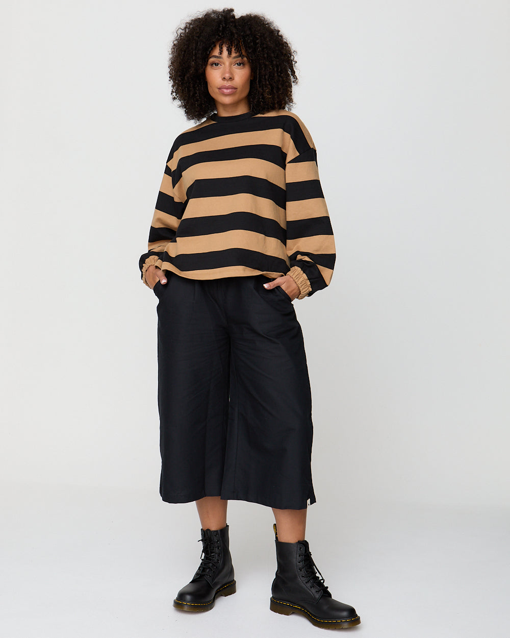 Person wearing a black and beige striped sweater with black pants and boots on a white background