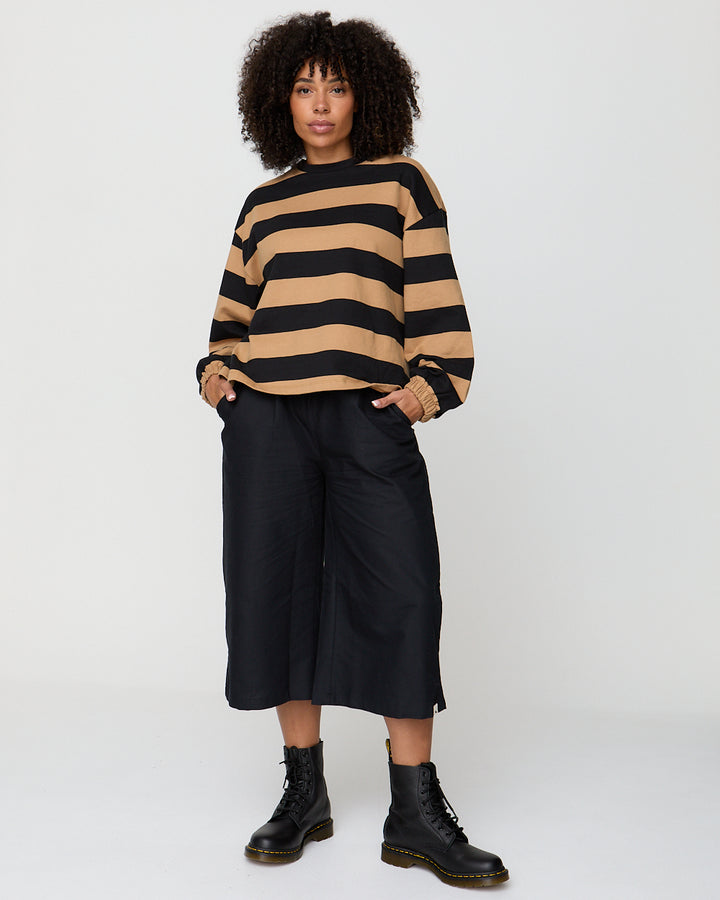 Person wearing a black and beige striped sweater with black pants and boots on a white background
