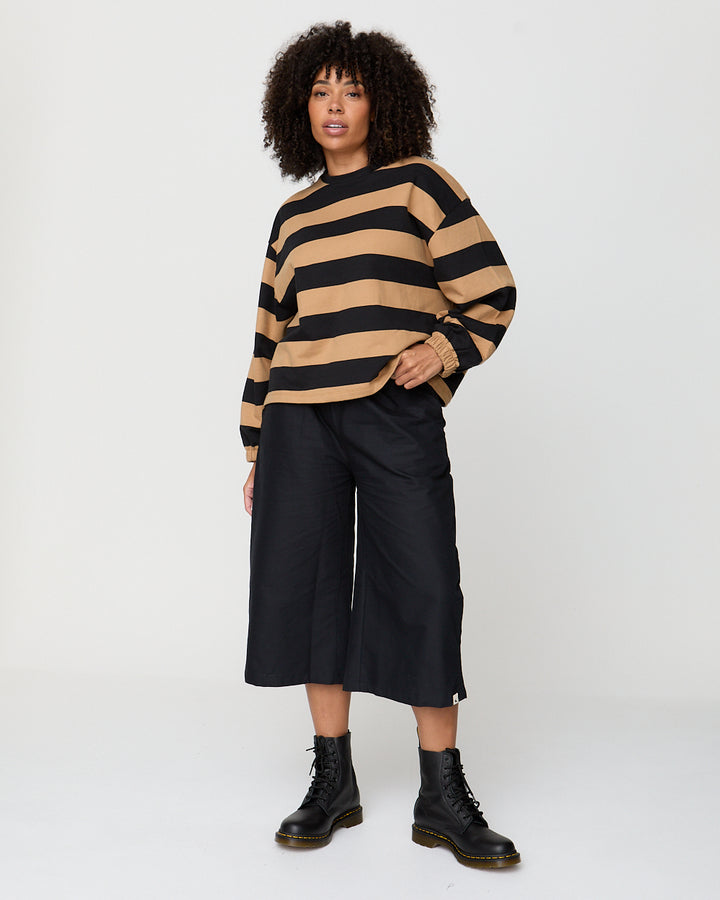 Woman wearing a black and beige striped sweater with black pants and boots on a white background