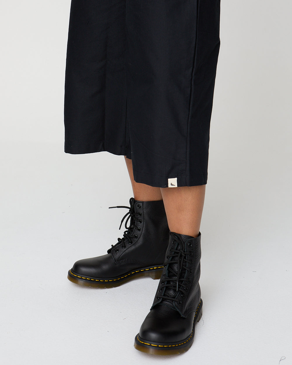 Person wearing black boots with yellow laces on a white background