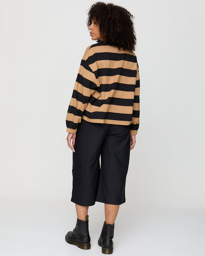 Person wearing a black and beige striped sweater with black pants on a white background