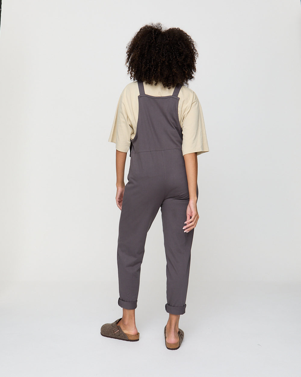 Person wearing gray overalls and a beige shirt on a white background