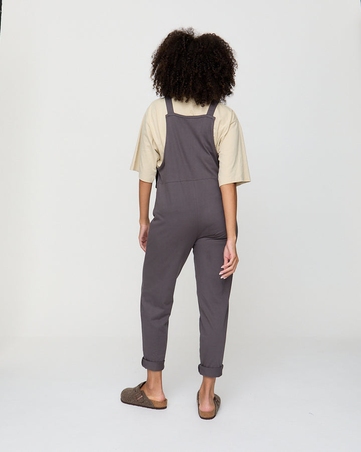 Person wearing gray overalls and a beige shirt on a white background