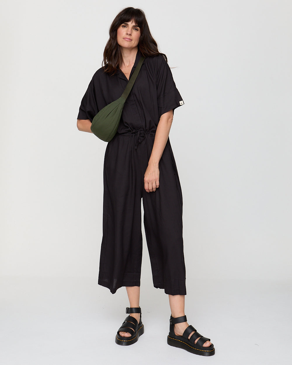 Woman wearing a black jumpsuit with a green bag on a white background