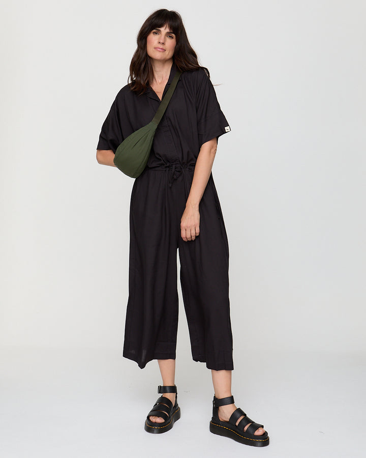 Woman wearing a black jumpsuit with a green bag on a white background