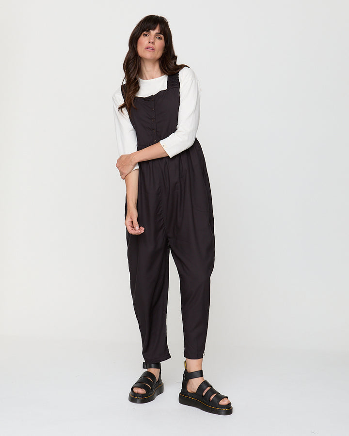 Woman wearing a black jumpsuit over a white shirt on a white background