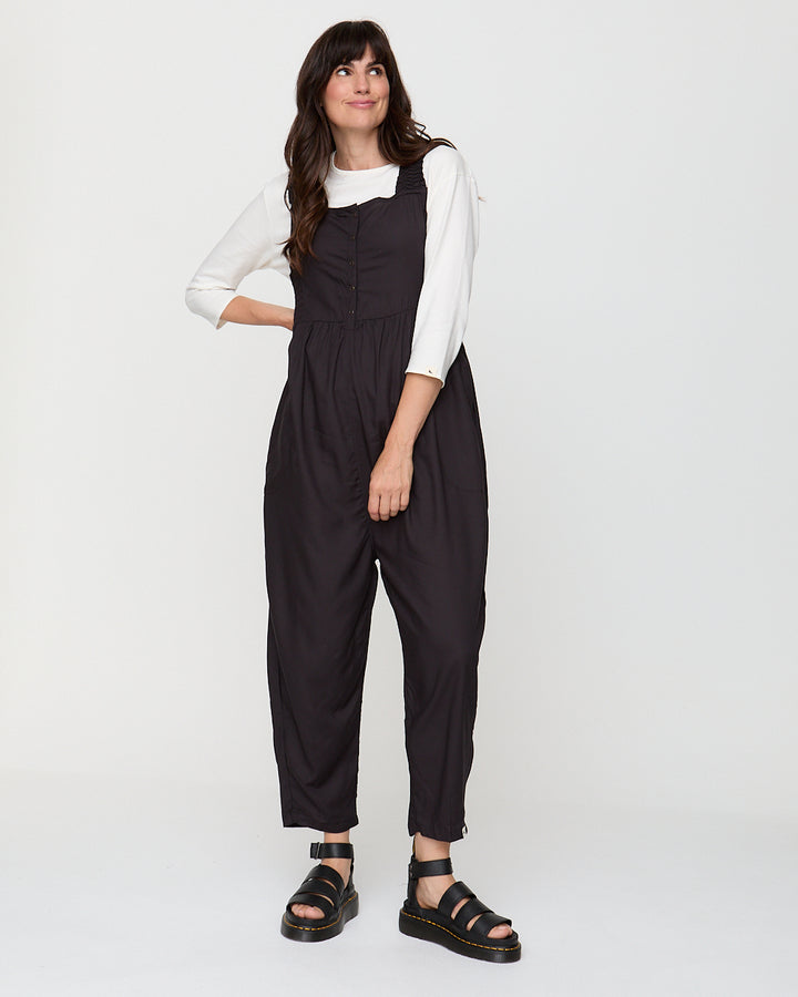 Woman wearing black overalls and a white shirt on a white background