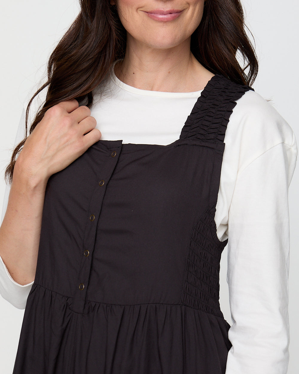 Woman wearing a black pinafore dress over a white shirt against a white background