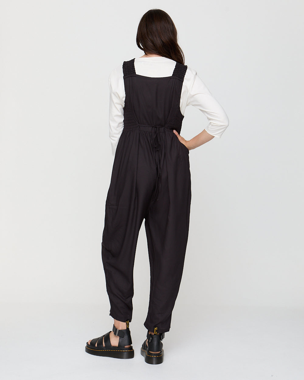 Person wearing a black jumpsuit with a white shirt underneath on a white background