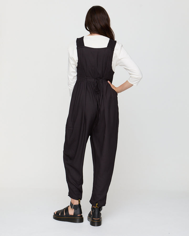 Person wearing a black jumpsuit with a white shirt underneath on a white background