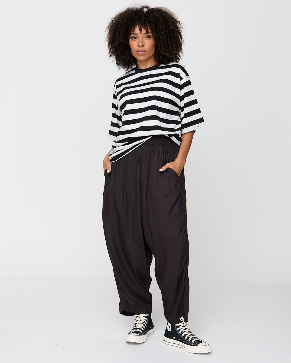 Person wearing a black and white striped shirt and black pants with Converse shoes on a plain background